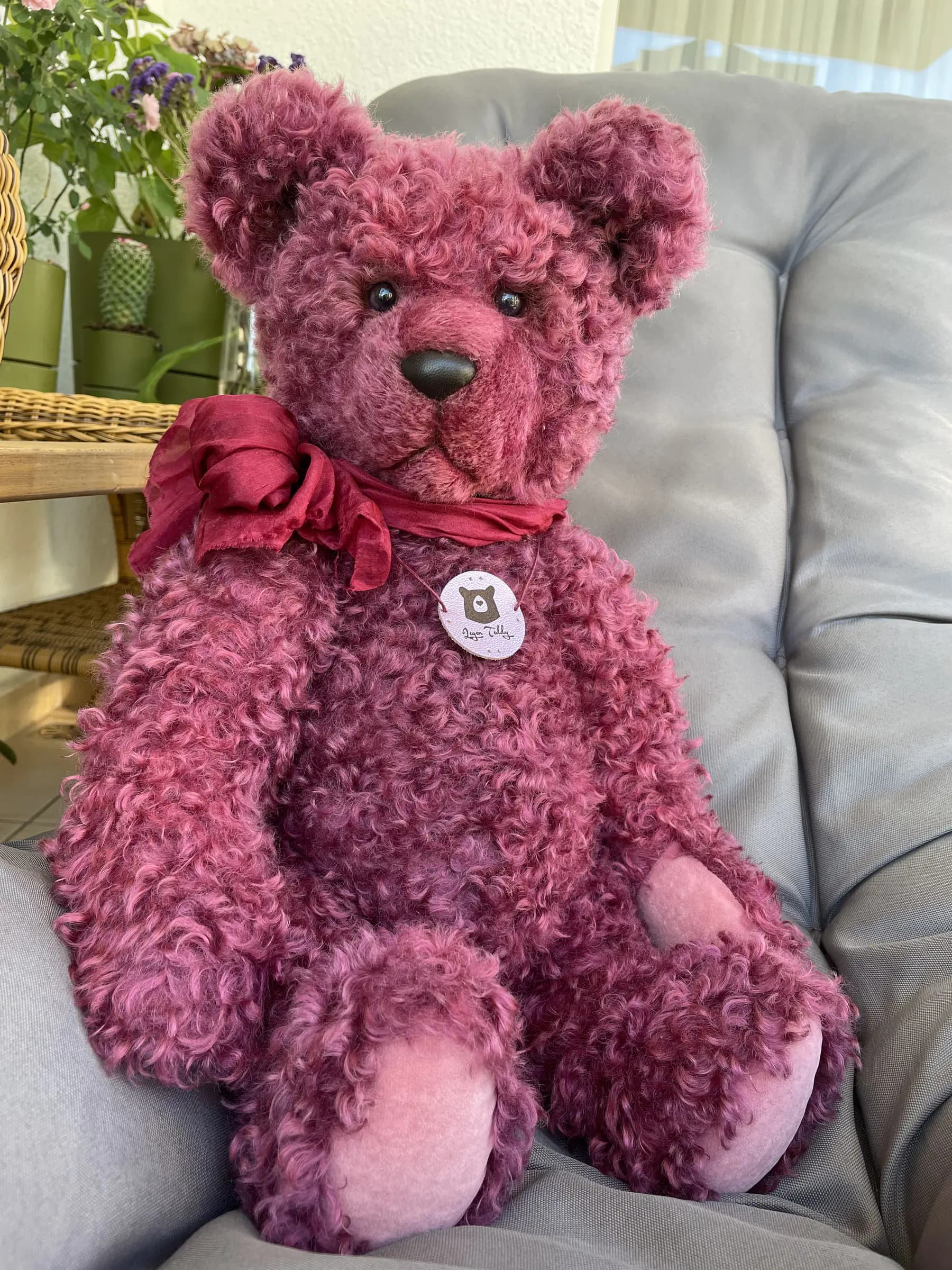 Uwe, a berry-pink mohair artist bear with a velvet bow, seated on a pale blue chair