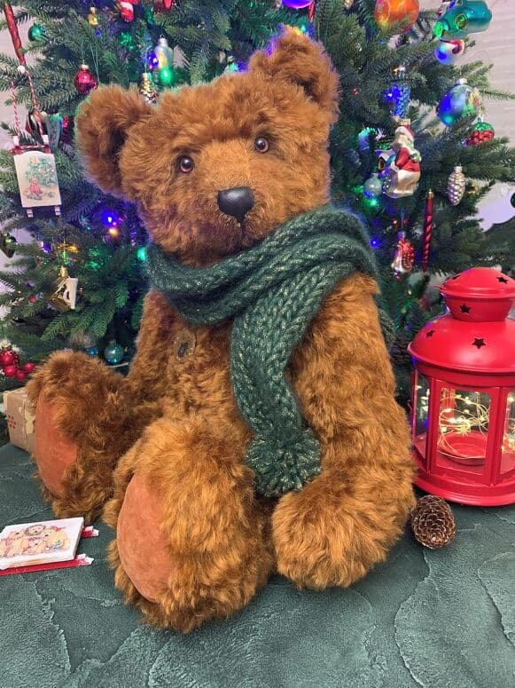 Ginger, a russet mohair artist bear, seated by a Christmas tree