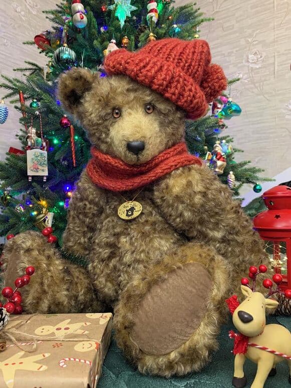 Bosphorus, a taupe mohair artist bear, seated in a red hat and scarf